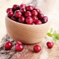 A wooden bowl filled with red cranberries sits on a table, with some cranberries spilling over.