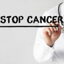 A doctor writing Stop Cancer Now on a clear wall in black marker.