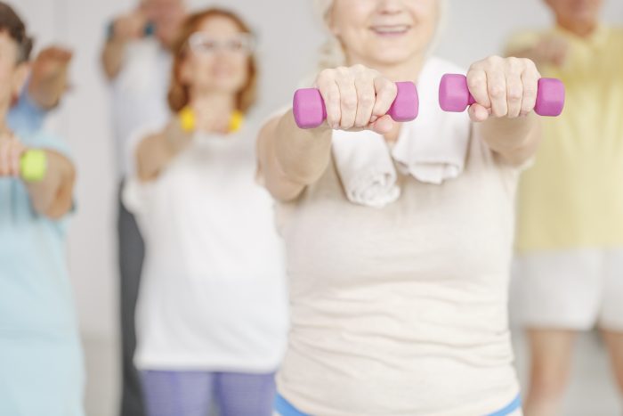 Older women in an exercise class do arm lifts with light free-weights