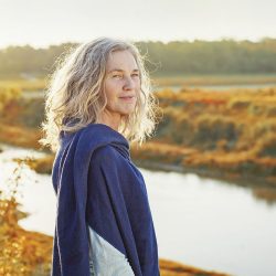 An older woman stands peacefully beside a lake in autumn.