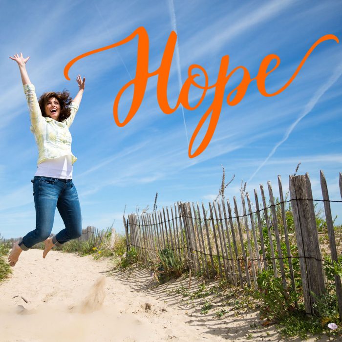 A woman jumps for joy on a beach and the word Hope is in orange in the right hand corner.