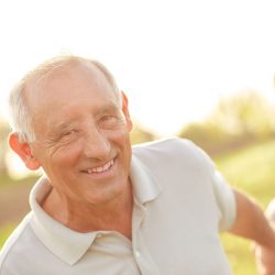 An older man smiles outside in the sun.