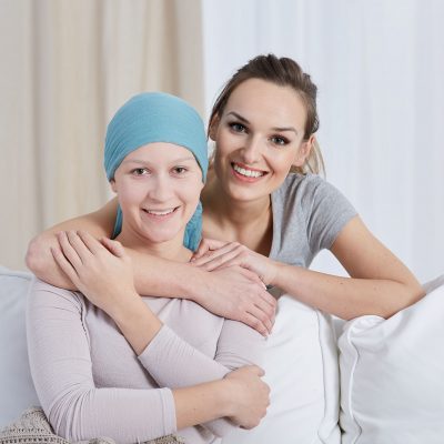 Two women smile for a photo, one has cancer and a scarf around her head.