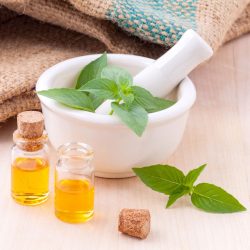 Two aromatherapy bottles are placed next to a mortar and bowl with mint leaves.