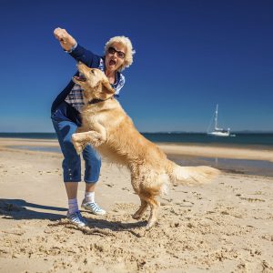 An older woman plays catch with her dog on the beach with joy.